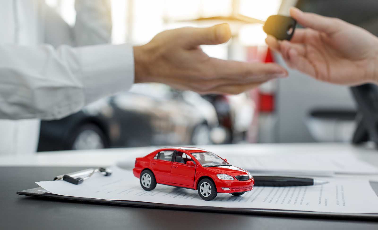 Toy car on legal documents with two hands passing car keys behind