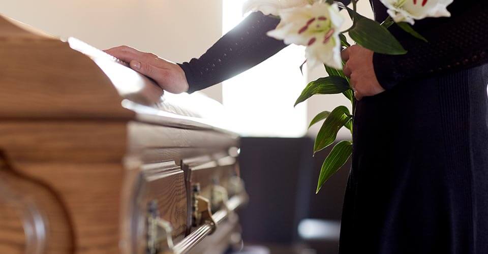 Hand placed on a casket with a handful of white lilies