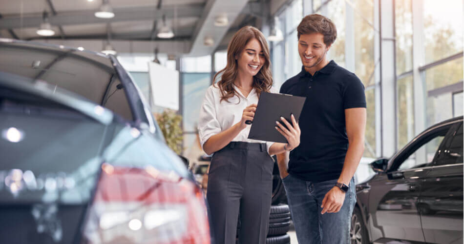 Young man looking over dealership paperwork with a young woman in a car dealership