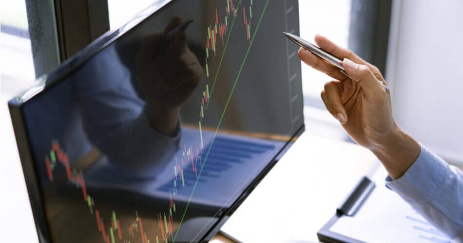 Hand using a pen to point at computer screen showing stock charts